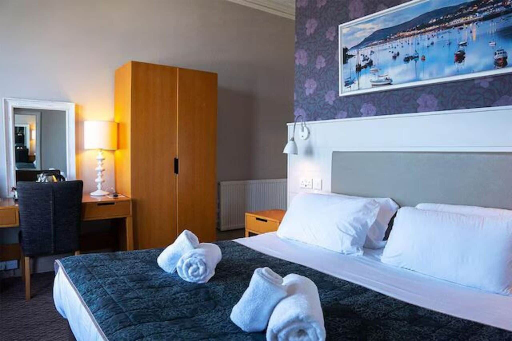 Une chambre d’hôtel avec un lit, un bureau, une armoire, un tableau au mur et une fenêtre.