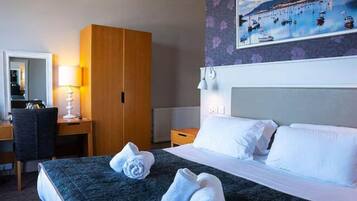 Une chambre d’hôtel avec un lit, un bureau, une armoire, un tableau au mur et une fenêtre.