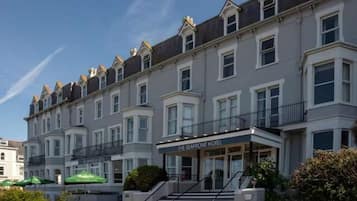 A multi-story hotel with a classic architectural style, featuring a prominent entrance with steps and a sign reading 'The Seafront Hotel'.