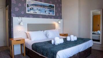 Una habitación de hotel con una cama, dos mesitas de noche, un cabecero, un cuadro y un espejo.