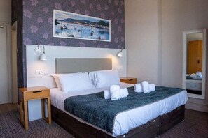 Ett hotellrum med en säng, två sängbord, en sänggavel, en tavla och en spegel.