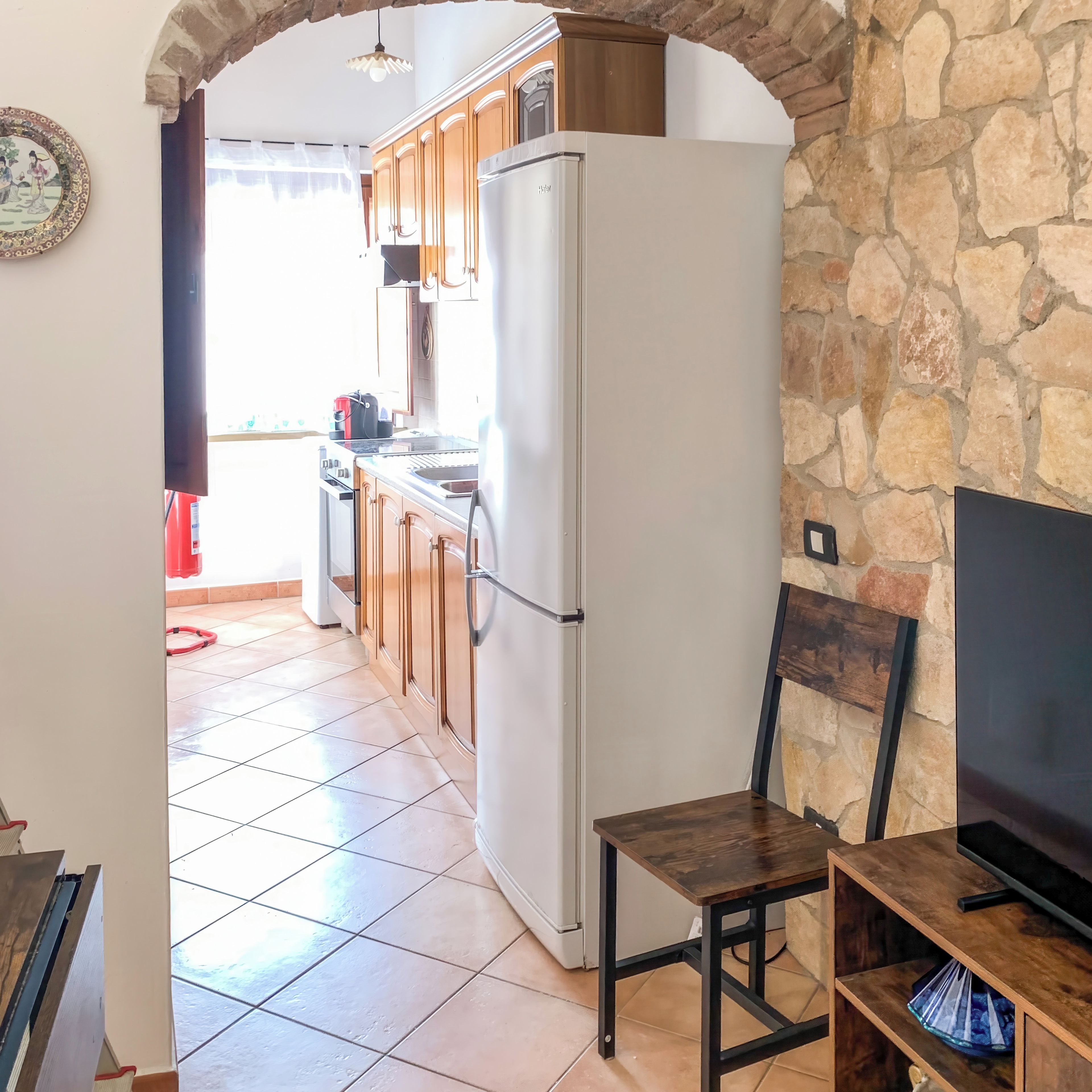 A kitchen with a white refrigerator, wooden cabinets, a tiled floor, and a stone wall.
