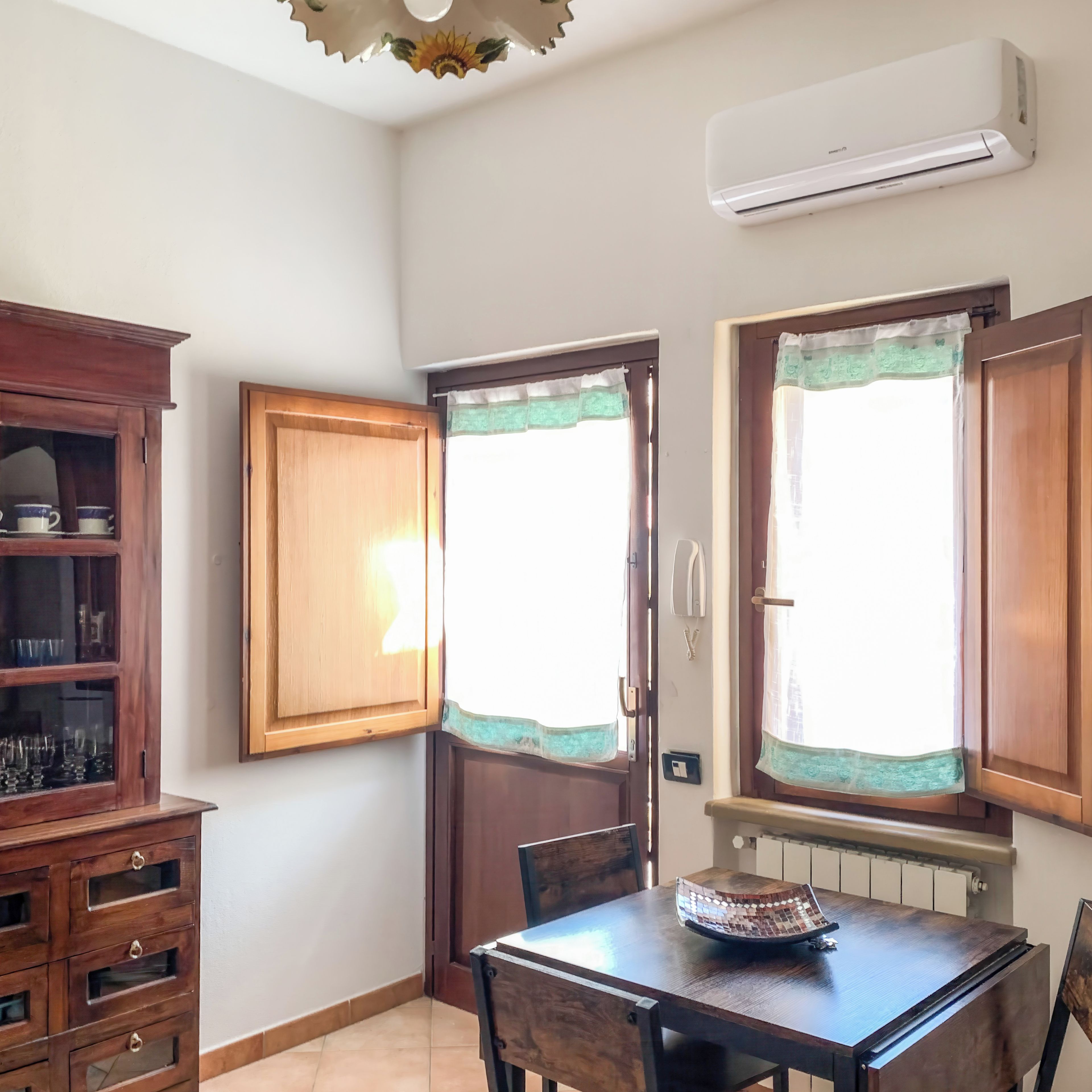 A dining area with a wooden table, chairs, a cabinet with glass doors, and an air conditioning unit mounted on the wall.
