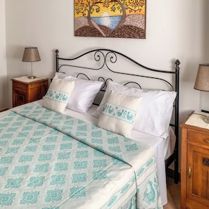A neatly made bed with patterned bedding, a decorative wall painting, and a bedside table with a lamp. - Domo Juanna (Laconi)