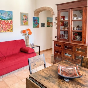 A living room with a red sofa, a wooden cabinet with glass doors, and various artworks on the walls. - Domo Juanna (Laconi)