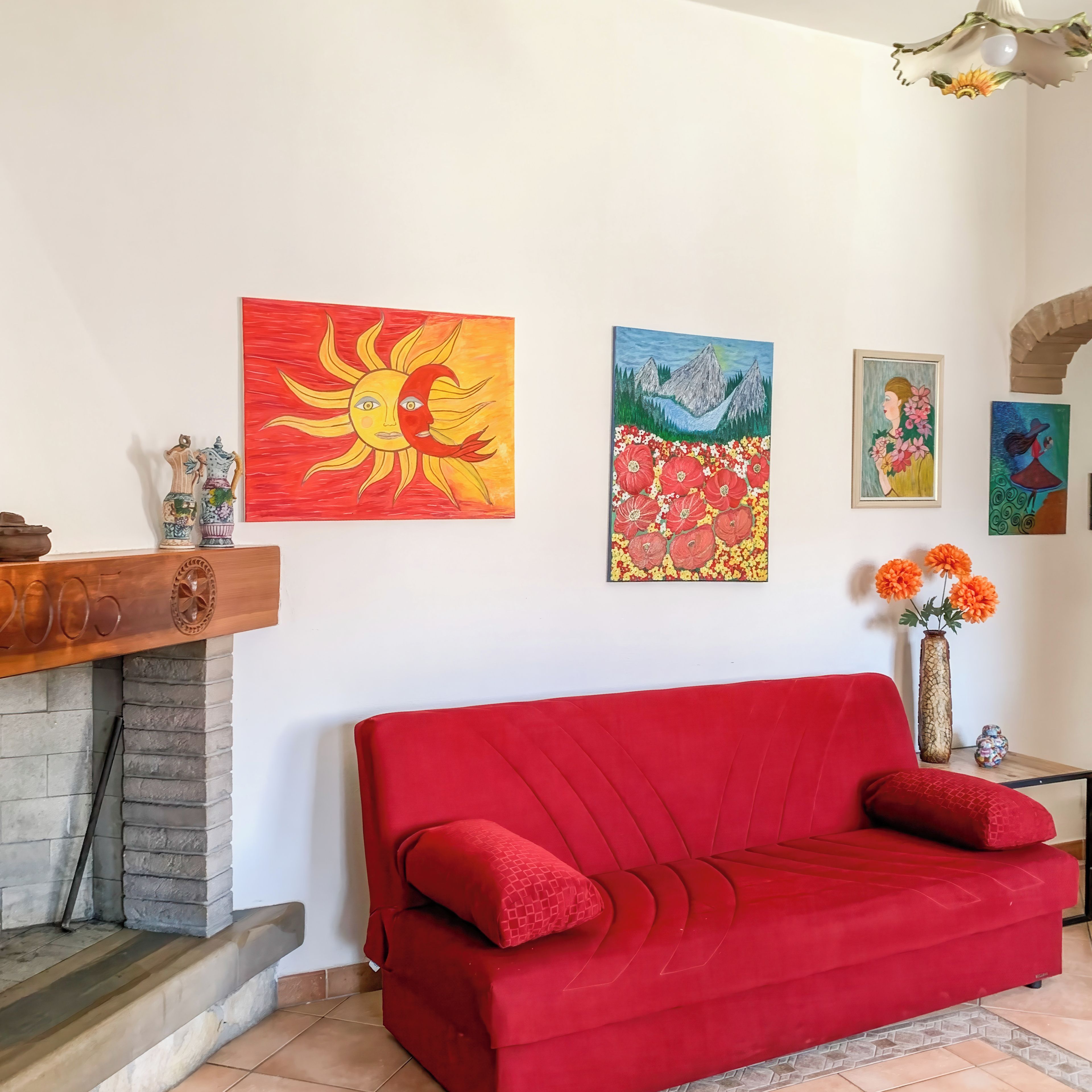 Un salon avec un canapé rouge, une cheminée et diverses œuvres d’art accrochées au mur.