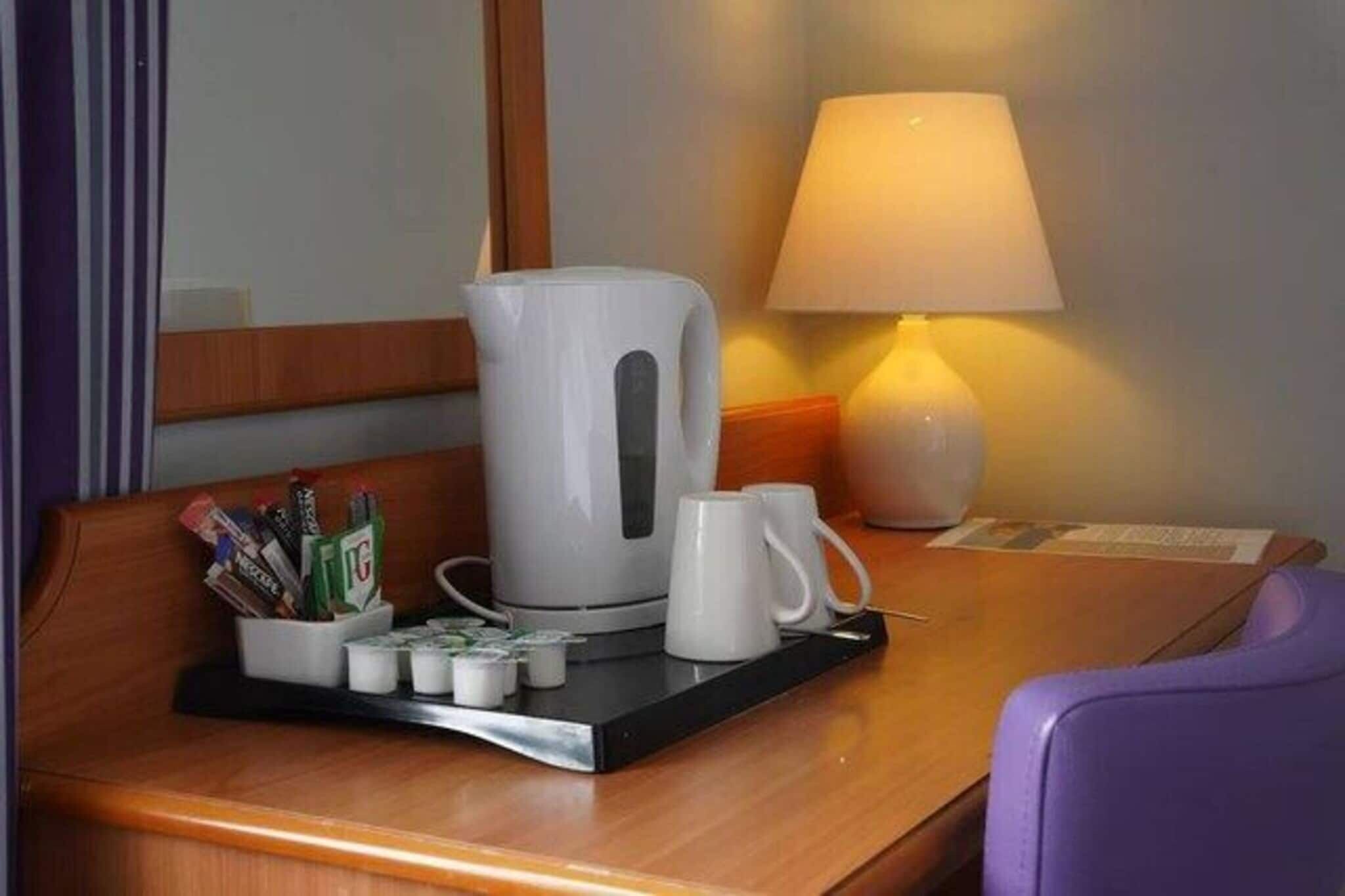 A hotel room with a coffee maker, a mug, and a tray with pens and tissues.