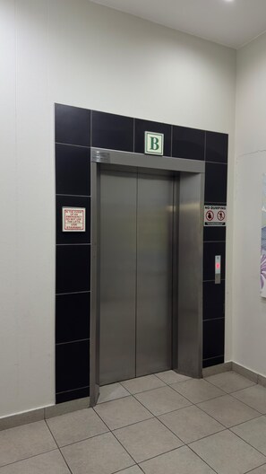Ein Aufzug mit einem 'B'-Schild darüber, Notfall-Kontaktinformationen und einem Verbotsschild gegen das Abladen von Müll.