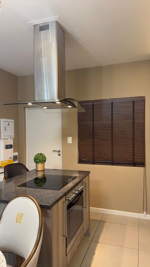 A modern kitchen with a stainless steel range hood, a built-in oven, and a granite countertop. - Cozy 1-bedroom apartment in delightful Sandton with AC (Sandton)