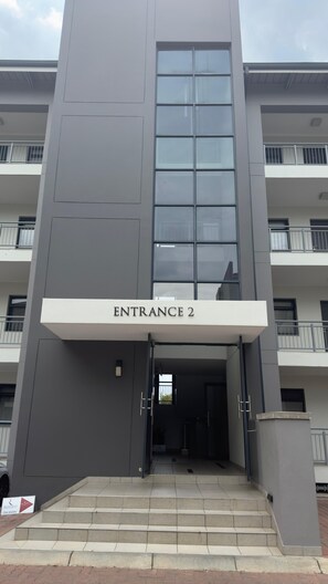 A modern building with a sign reading 'ENTRANCE 2' above the entrance. - Cozy 1-bedroom apartment in delightful Sandton with AC (Sandton)