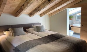 A bedroom with a large bed, a wooden ceiling, and a view of a bathroom. - CENTRAL ZERMATT PENTHOUSE WITH SUNNY BALCONY & MATTERHORN VIEWS (Zermatt)
