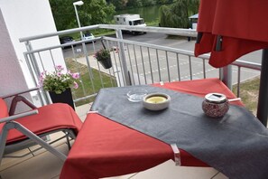 A balcony with a table, chairs, and a view of a road and greenery. - Holiday apartment with 1 bedroom (Traben-Trarbach, Deutschland)