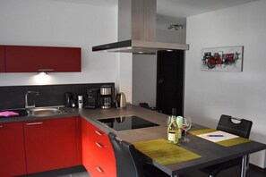 Una cocina moderna con armarios rojos, un lavamanos de acero inoxidable y una zona de comedor con una mesa dispuesta para dos.