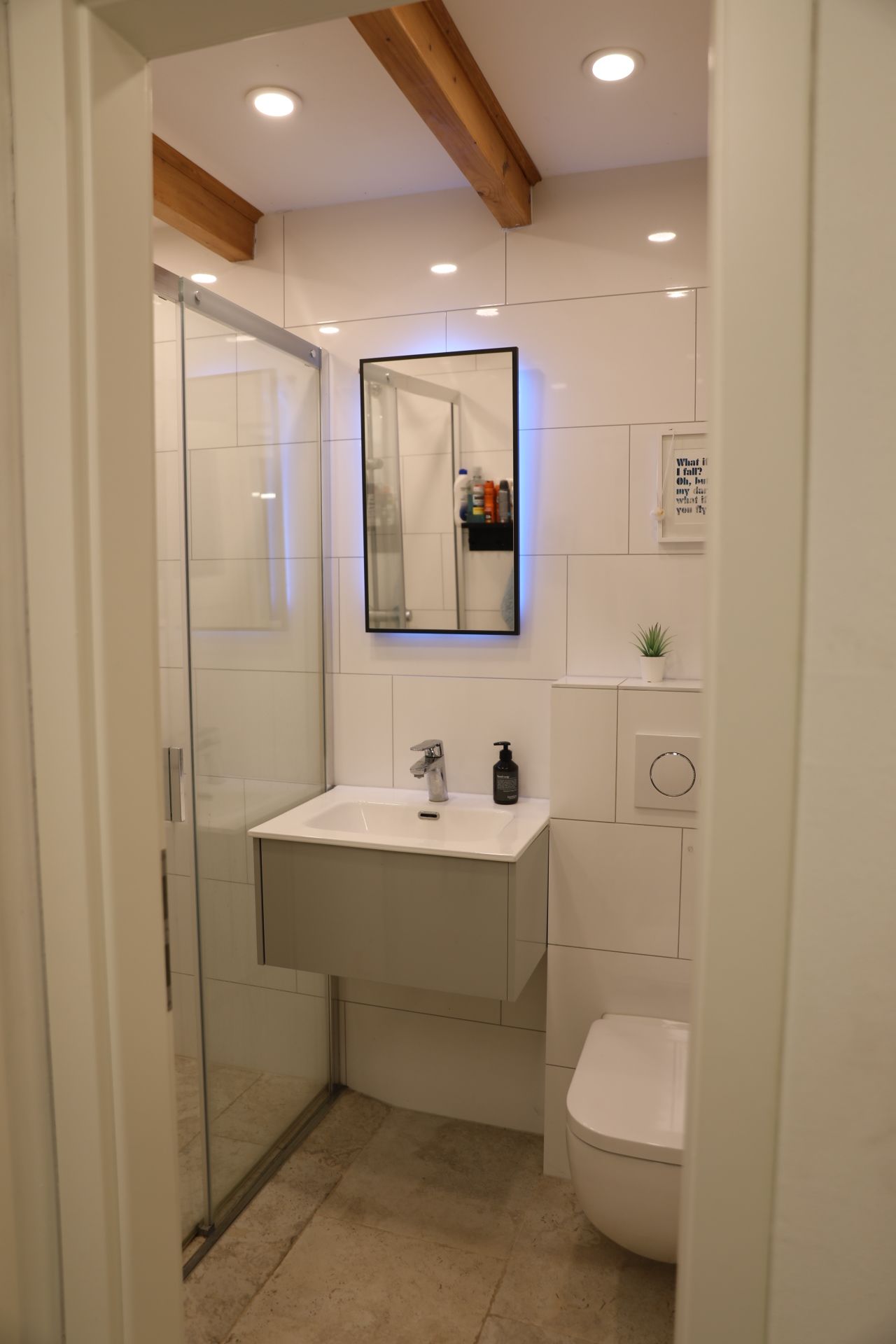 Ein modernes Badezimmer mit Duschabtrennung aus Glas, einem weißen Waschbecken mit Spiegel darüber und einer Toilette.