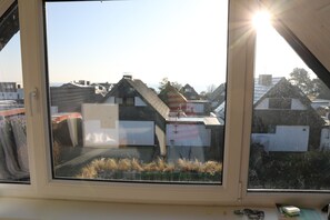 Udsigt fra et vindue med klar himmel, der viser et boligområde med huse og et vandområde i det fjerne.