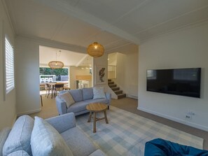A modern living room with a sofa, a round wooden stool, a flat-screen TV, and a staircase leading to another level. - The Dolls House - Boutique Bluff Hill Cottage (Napier)