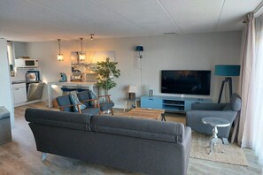 Ein modernes Wohnzimmer mit einer Couch, einem Fernseher und einem Essbereich mit Tisch und Stühlen.