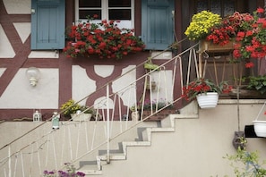 A staircase with a white railing, a wall with a half-timbered design, and flower boxes with red and yellow flowers. - Bär's holiday apartment (Eichstetten)
