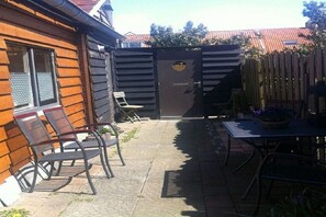 A patio area with a table and chairs, a wooden fence, and a door with a logo. - Holiday apartment with 2 bedrooms (Westkapelle)