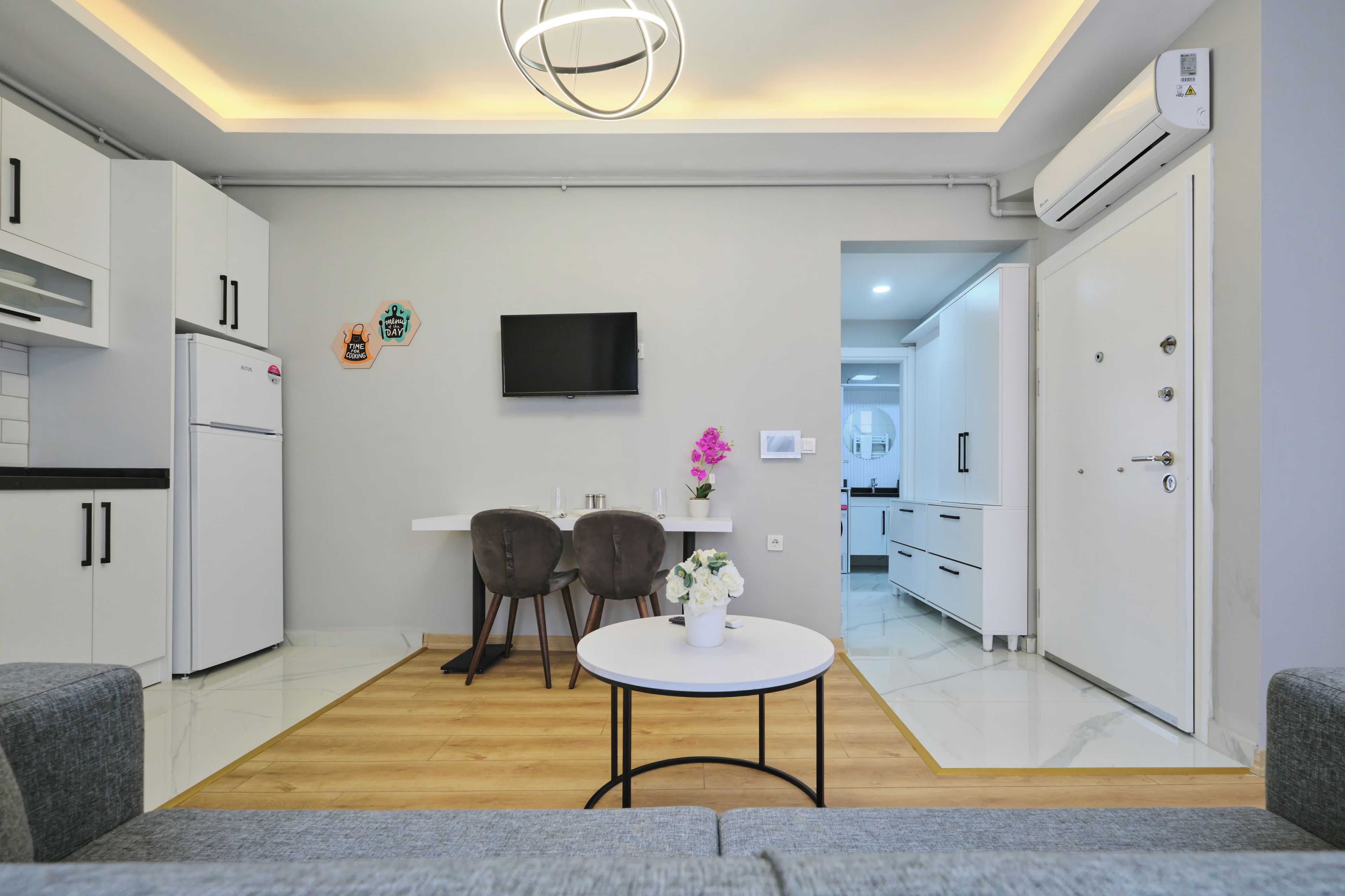 A modern kitchen with white cabinets, a built-in oven, and a flat-screen TV mounted on the wall.