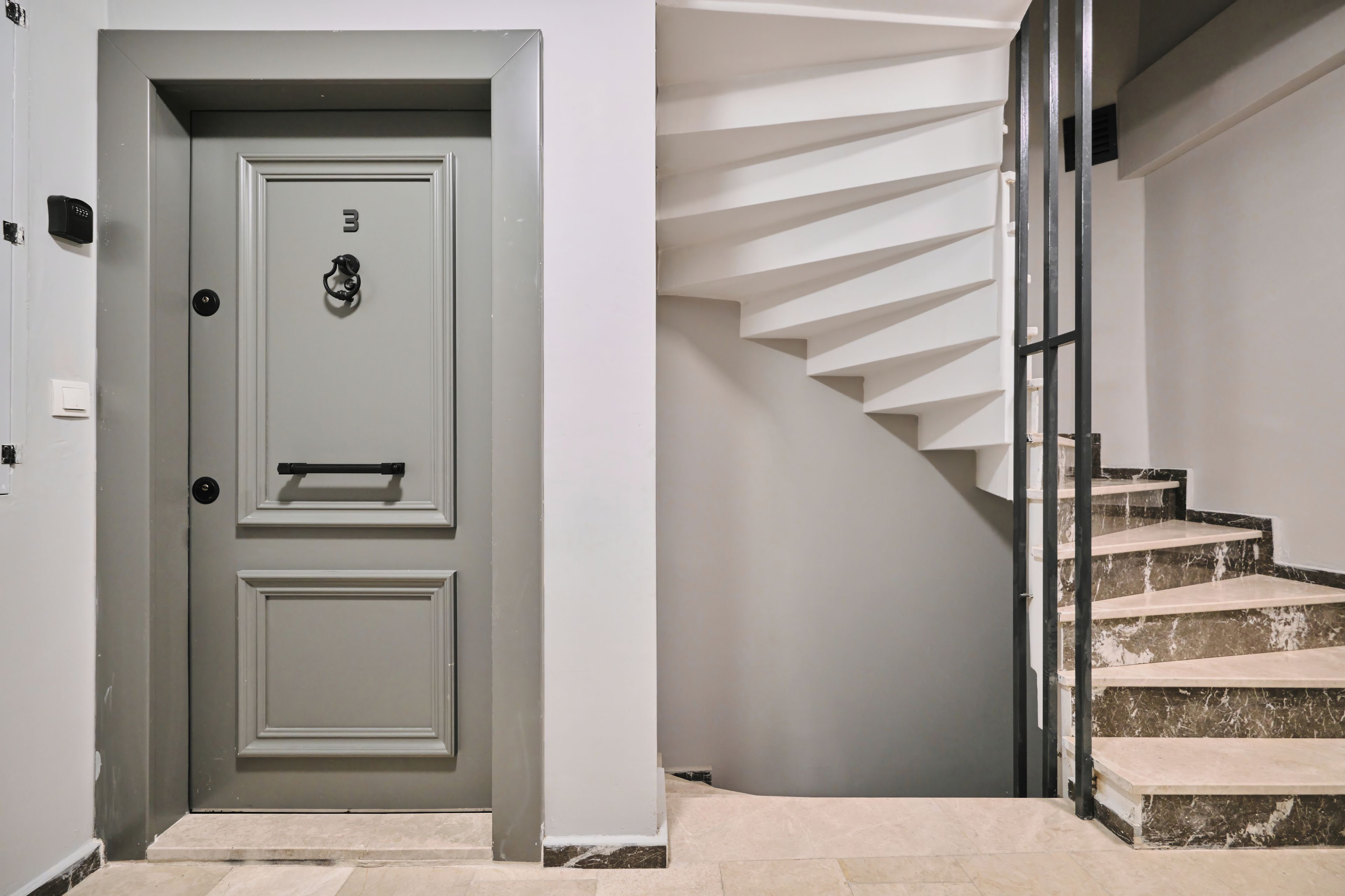 Un interno moderno con una porta grigia, una scala con gradini in marmo e un design pulito e minimalista.