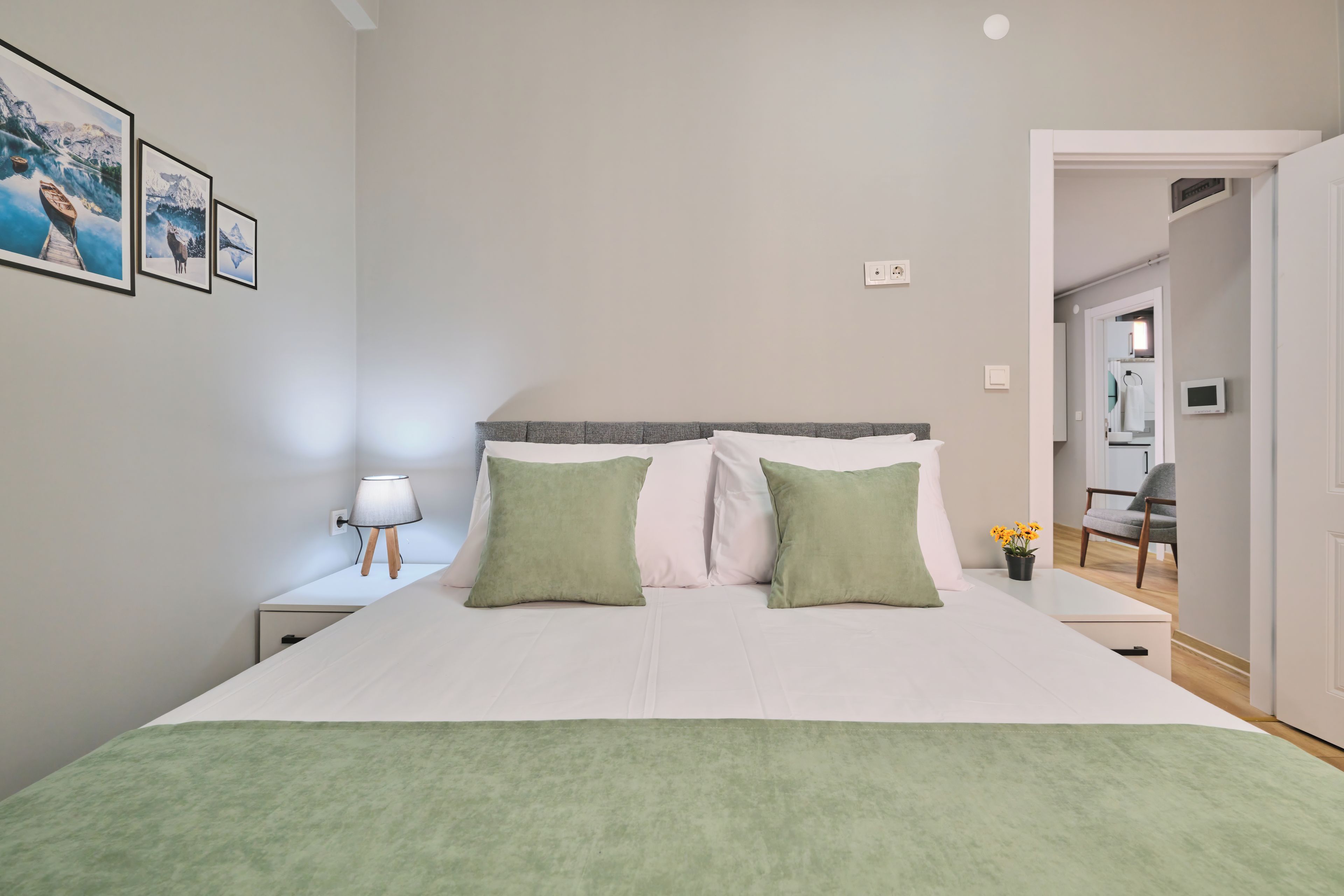 A bedroom with a bed, pillows, a nightstand, a lamp, and a wall with framed pictures.