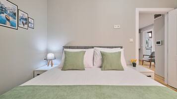 A bedroom with a bed, pillows, a nightstand, a lamp, and a wall with framed pictures.