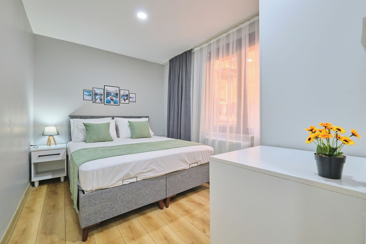 A bedroom with a bed, bedside table, lamp, and a potted plant.