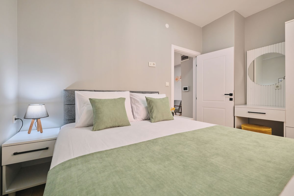 A neatly arranged bedroom with a bed, bedside table, lamp, and a door leading to another room.