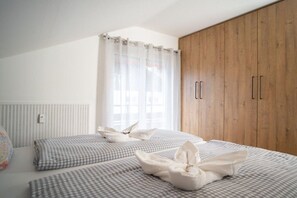 A bedroom with a large wardrobe, a bed with checkered bedding, and a window with sheer curtains. - Holiday apartment with 2 bedrooms (Bad Hindelang)
