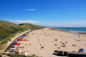 Ein Strand mit Zelten und Badegästen, einem klaren Himmel und einer Küstenlinie.