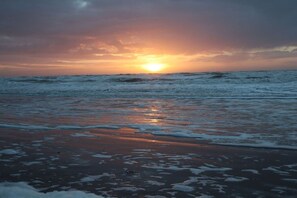 Een strand met golven en een ondergaande zon.