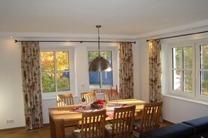 A dining area with a wooden table, chairs, a hanging pendant light, and windows with curtains. - Holiday home in Brilon with swimming pool (Brilon)