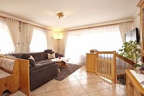 A living room with a sofa, a coffee table, a TV, and a staircase. - Holiday apartment with 2 bedrooms (Grainau, Oberbayern)