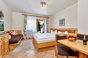 A bedroom with a bed, a desk, a chair, a TV, and a window with curtains. - Holiday apartment with 2 bedrooms (Grainau, Oberbayern)