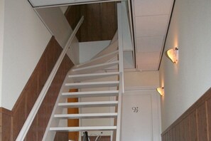 Una scala bianca con gradini in legno e un corrimano bianco, che conduce a una porta con il numero 98.