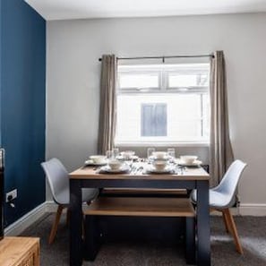 A dining area with a table set for four, two chairs on each side, a window with curtains, and a view of the outside. - Centraldarlington - House - Stay7 - Nearhippodrome (Darlington)