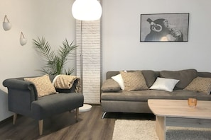 A modern living room with a grey sofa, a smaller armchair, a coffee table, and a floor lamp. - Coach house in the Villa Cues (Benkastel-Kues)