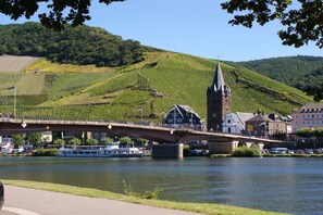 A bridge over a river with vineyards on the hillside, a historic building, and a boat. - Coach house in the Villa Cues (Benkastel-Kues)