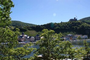 Eine Stadt am Flussufer mit Gebäuden, ein Hügel mit Grünflächen und ein klarer Himmel.