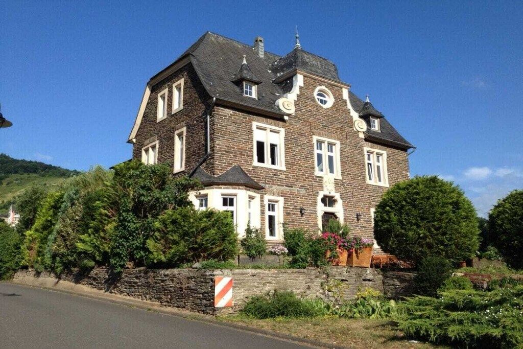 A large, two-story stone house with a prominent gabled roof, multiple windows, and a well-maintained garden.