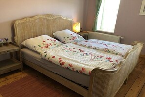 A double bed with a floral bedspread, a bedside table with a lamp, and a window with curtains. - House number 1 Moselblick (Reil)
