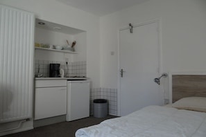 Ein kleines Zimmer mit Bett, einer kleinen Küchenzeile und einer Tür.