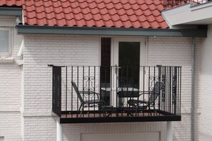 Un balcon doté d’une balustrade en métal noir, d’une table et de deux chaises.