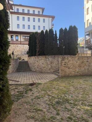 Un patio con muro de piedra, una escalera que lleva a un edificio y cielo despejado.