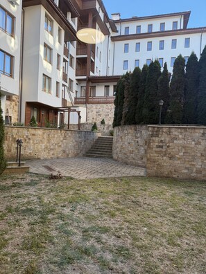 Edifício residencial com várias andares, fachada de pedra, escadaria central e um pátio gramado.