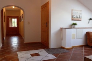 A hallway with a wooden door, a tiled floor, a rug, a plant, and a painting on the wall. - Holiday apartment with 2 bedrooms (Bischofswiesen)