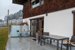 Eine Terrasse mit Tisch und Stühlen, einem Blumentopf und einer Glastür.