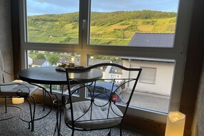 A room with a table and chairs, a window with a view of green hills and houses. - Brigitta Winery House -2- (Zell kaimt)
