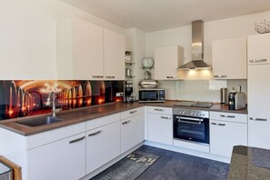 A modern kitchen with white cabinetry, a stainless steel range hood, a built-in oven, and a microwave. - Brigitta Winery House -2- (Zell kaimt)